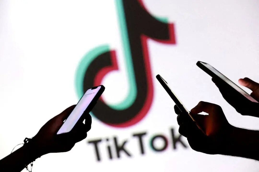插图显示青少年手持智能手机在 TikTok 徽标前摆姿势拍照